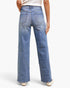 Rear view of a person wearing light blue wide-leg denim jeans with diagonal contrast stitching details, paired with a white top and beige shoes, against a light gray studio background.