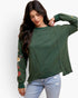 A woman wearing a dark green long-sleeve top with floral embroidery on one sleeve, paired with light blue jeans, against a plain white background.
