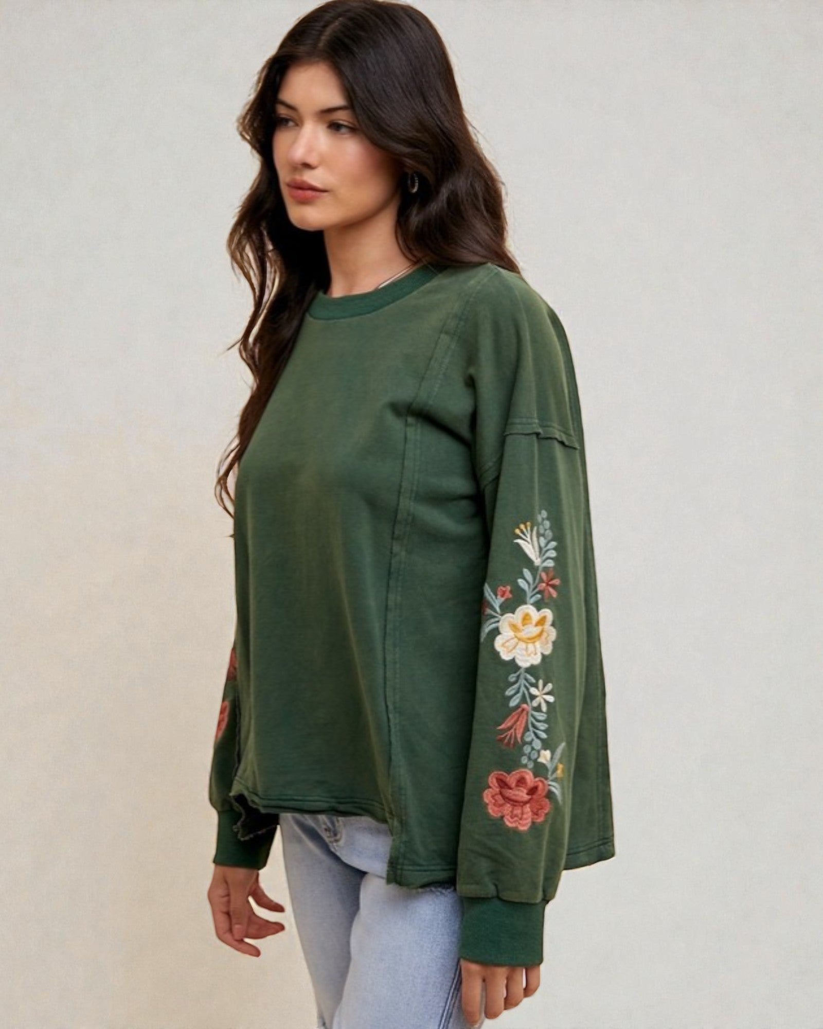 Woman wearing a green sweatshirt with floral embroidery on a plain background