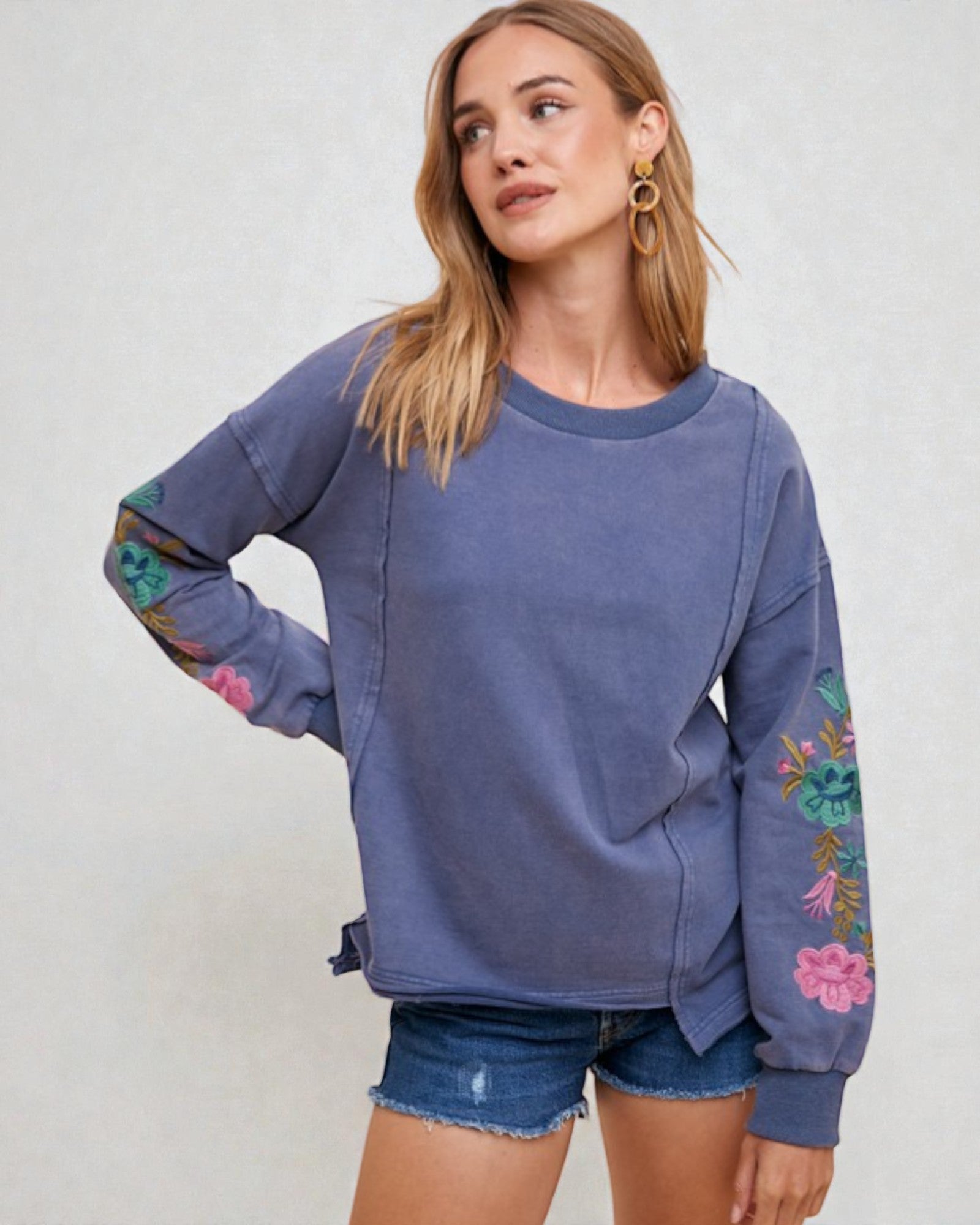 Woman wearing a blue sweatshirt with floral sleeves on a plain background