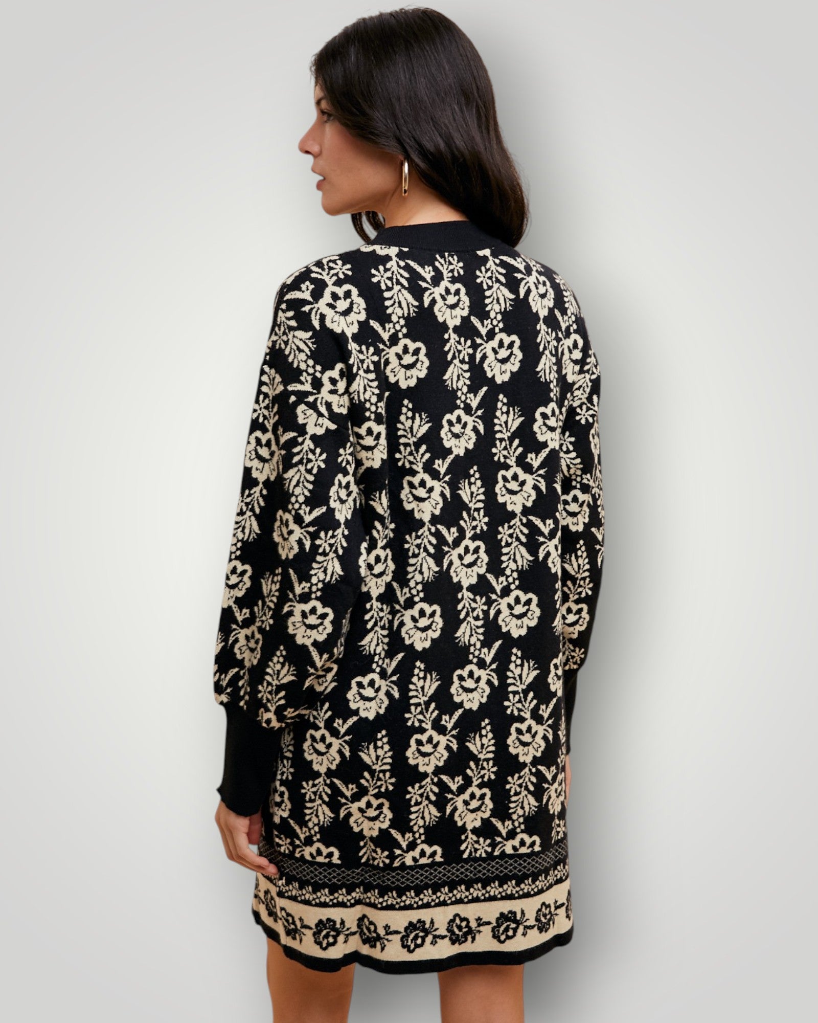 Woman wearing a black dress with beige floral pattern against a plain background