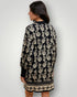 Woman wearing a black dress with beige floral pattern against a plain background