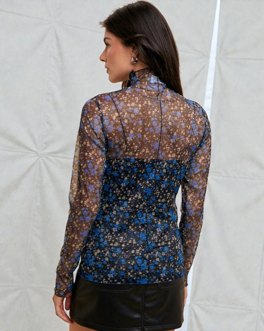 Woman wearing a floral patterned blouse with sheer sleeves against a neutral background