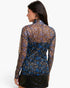 A woman shown from the back wearing a sheer long-sleeve mock-neck top with a dense floral print in brown, blue, and white, paired with a black skirt, against a plain white studio background.