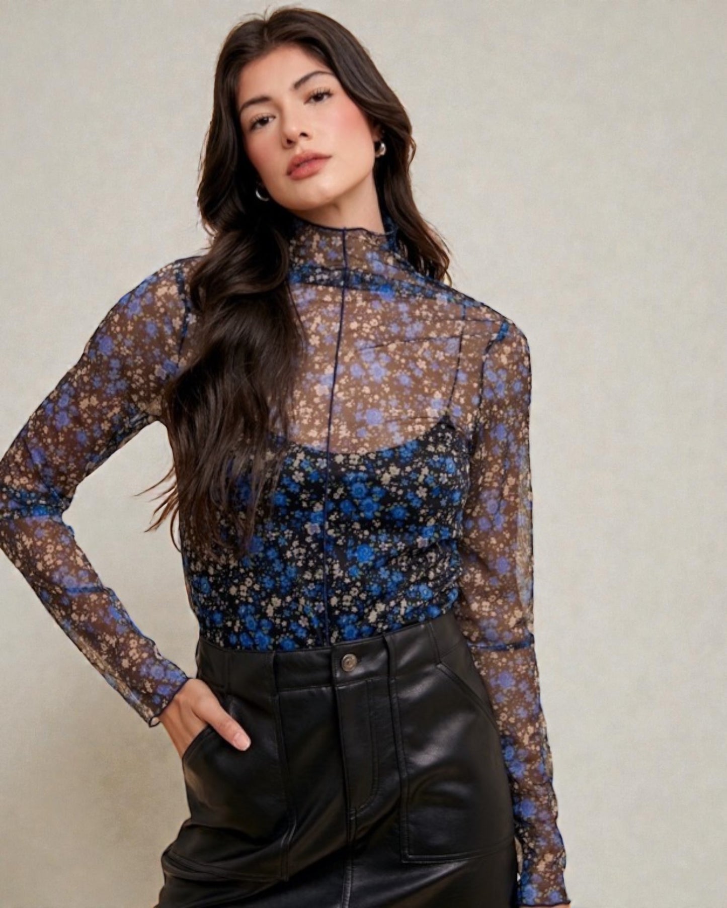Woman wearing a floral long-sleeve top and black pants against a neutral background