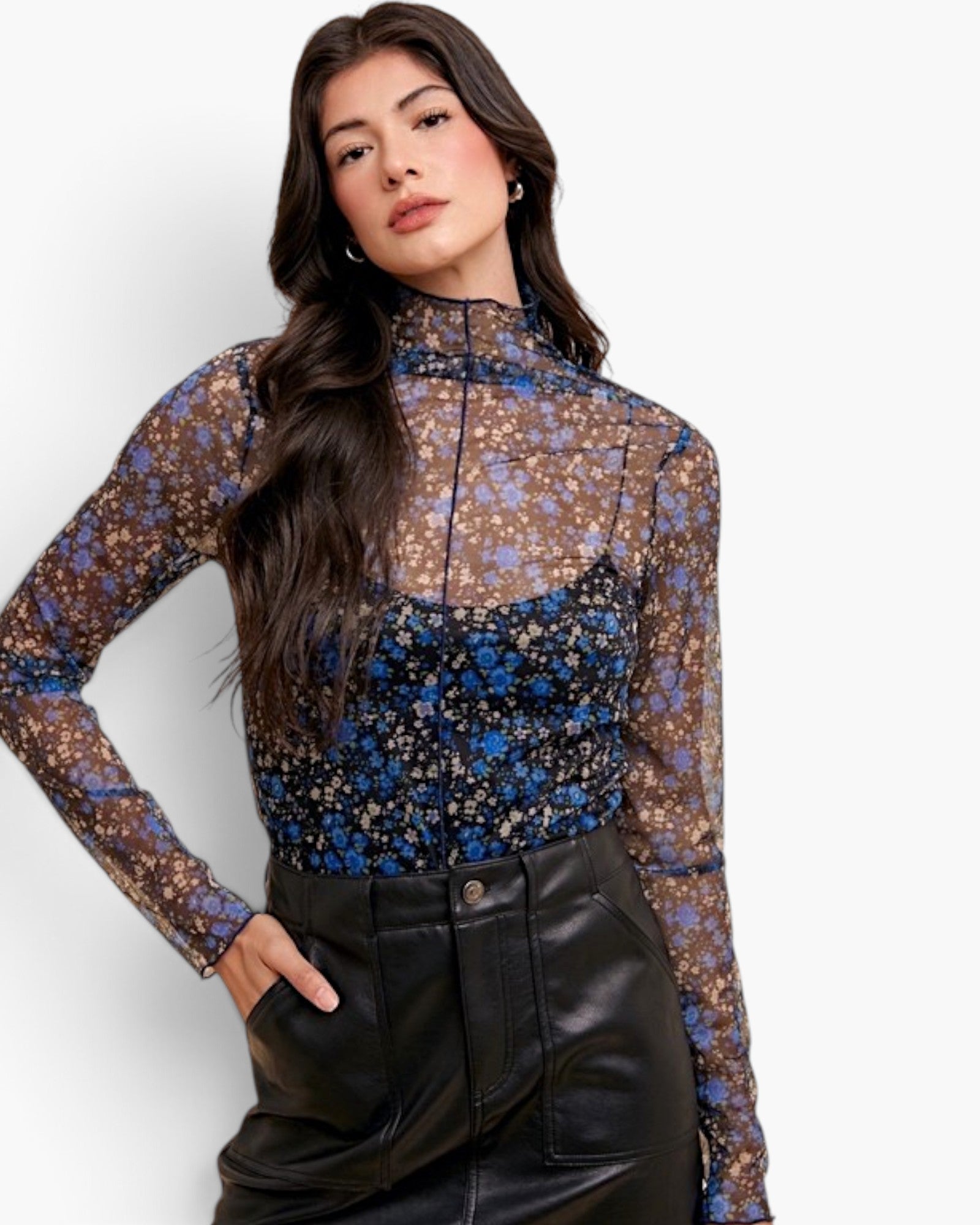 A woman modeling a sheer long-sleeve mock-neck top with a brown, blue, and beige floral pattern, paired with black faux-leather pants, against a plain white background.
