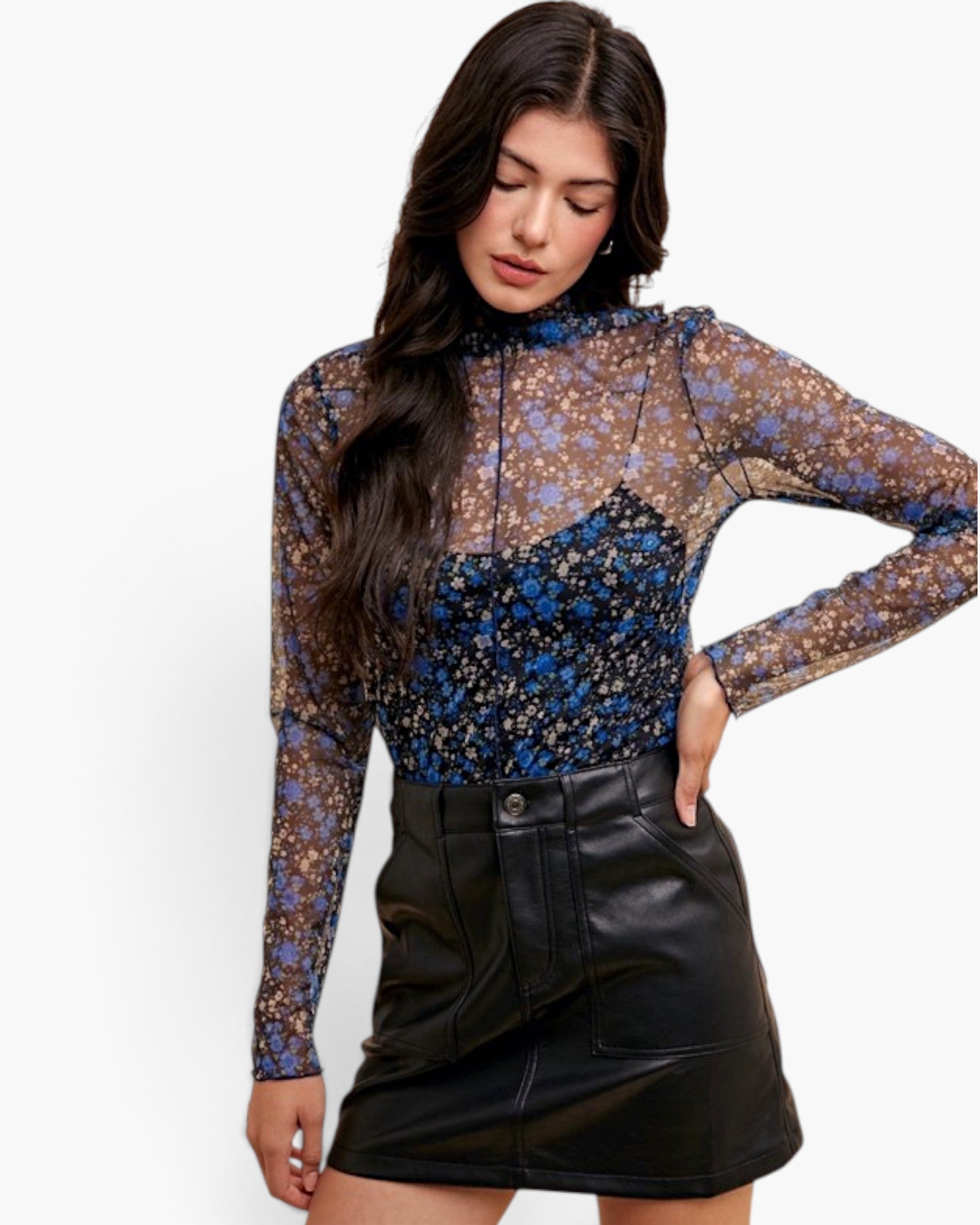 A woman modeling a sheer long-sleeve floral mock-neck top with blue and gold tones over a black underlayer, paired with a black faux-leather mini skirt, against a plain white background.