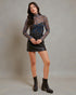 Woman wearing a floral long-sleeve top and black leather skirt with brown boots on a gray background