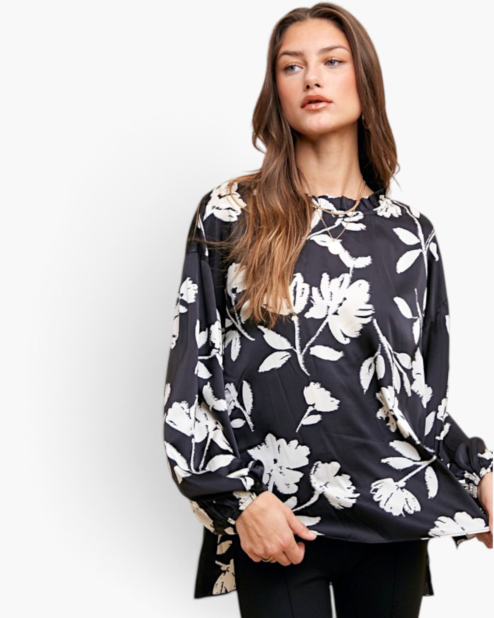 A woman wearing a black long-sleeve blouse with a white floral print, paired with black pants, photographed against a plain white studio background.