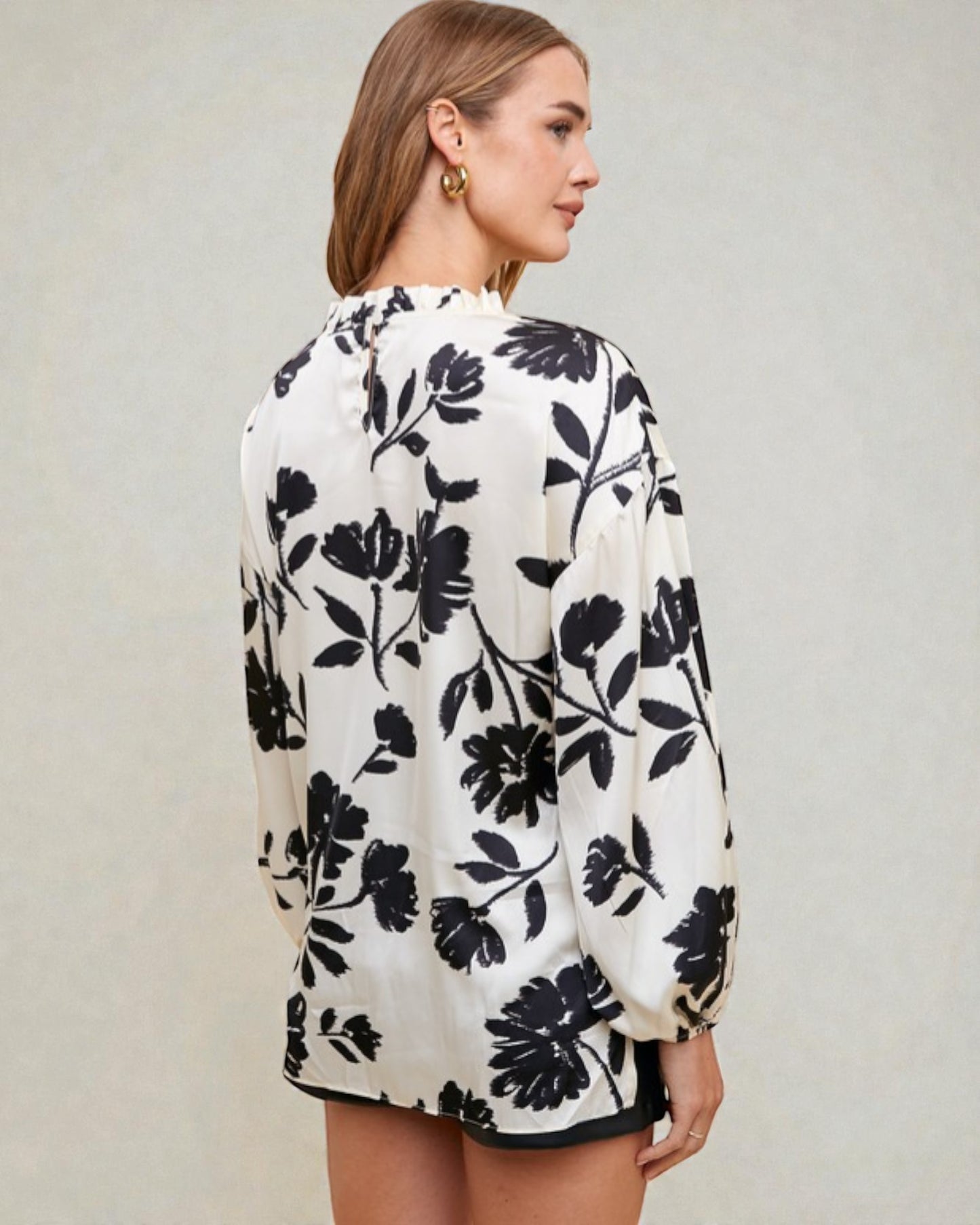 Woman wearing a white blouse with black floral pattern on a plain background