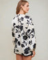 Woman wearing a white blouse with black floral pattern on a plain background