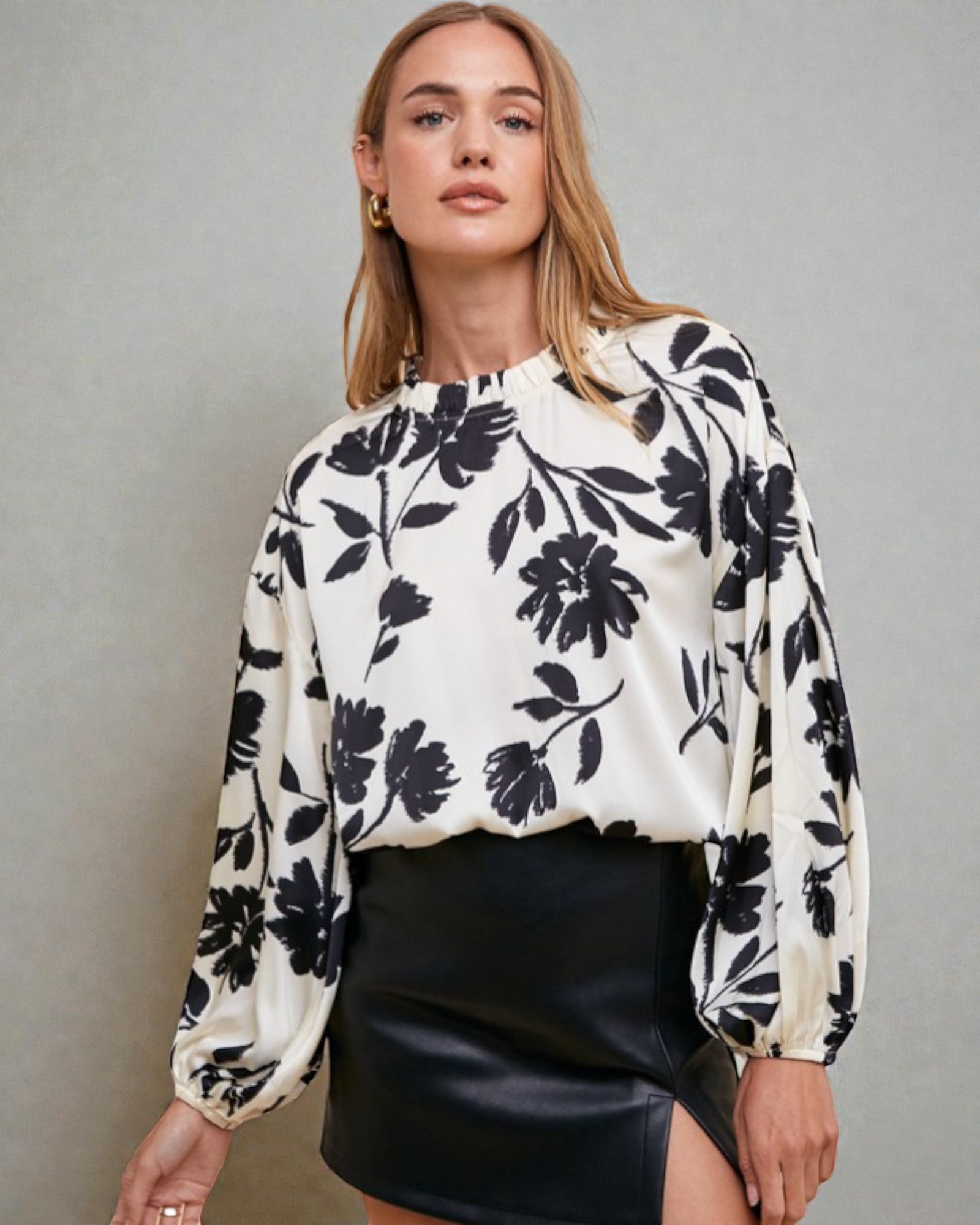 Woman wearing a white blouse with black floral pattern and black skirt against a gray background