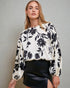 Woman wearing a white blouse with black floral pattern and black skirt against a gray background