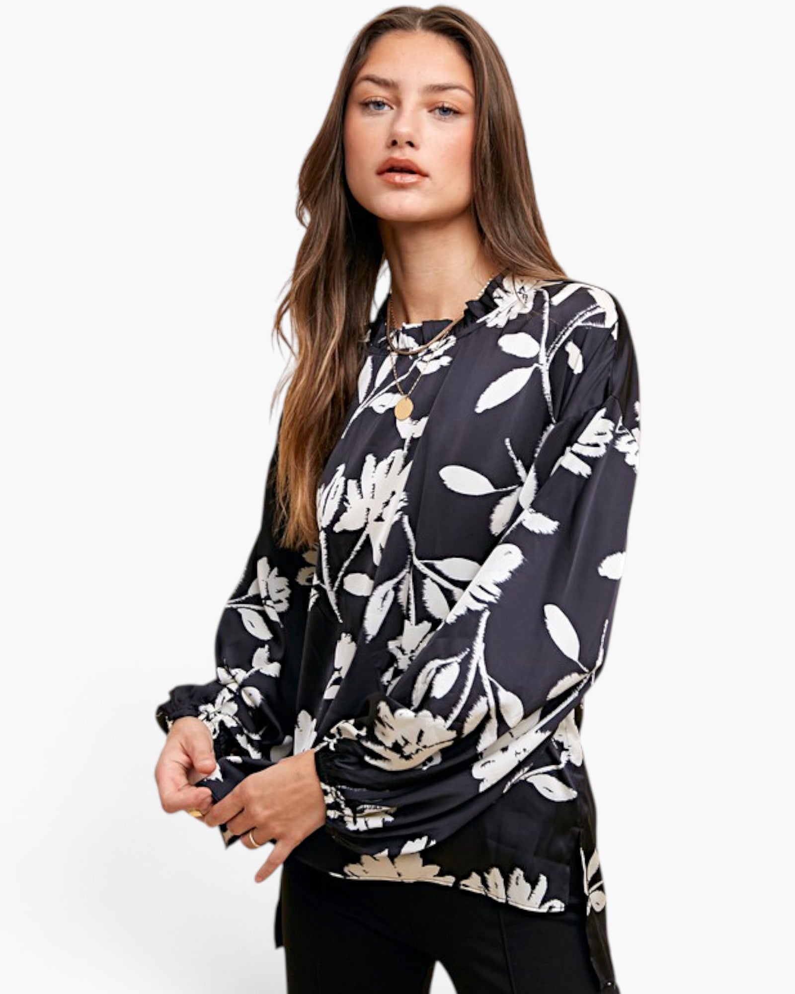 A woman modeling a black long-sleeve blouse with a white floral and leaf pattern, paired with black pants, against a plain white studio background.