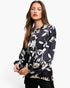A woman modeling a black long-sleeve blouse with a white floral and leaf pattern, paired with black pants, against a plain white studio background.