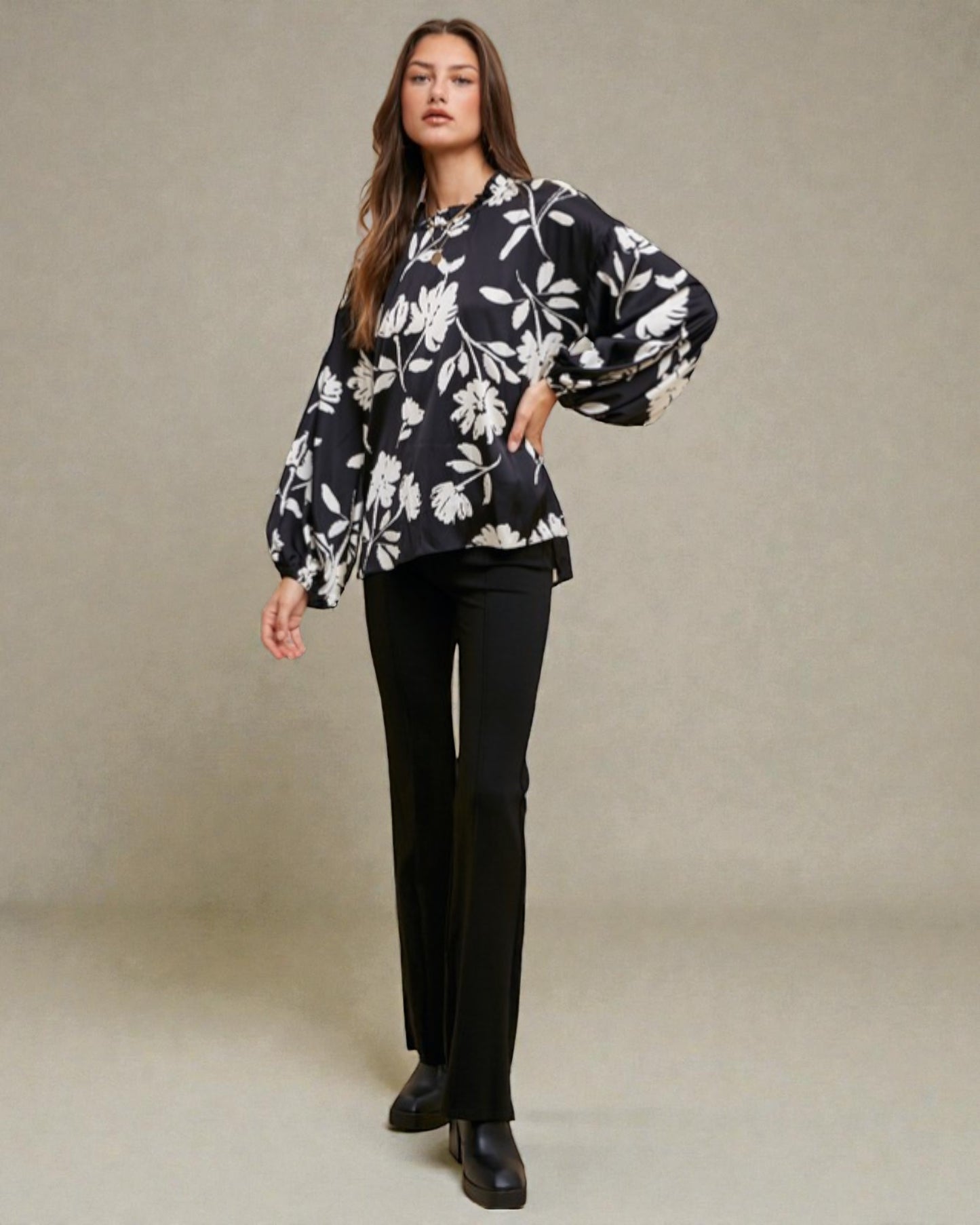 Woman wearing a black floral blouse and black pants against a beige background