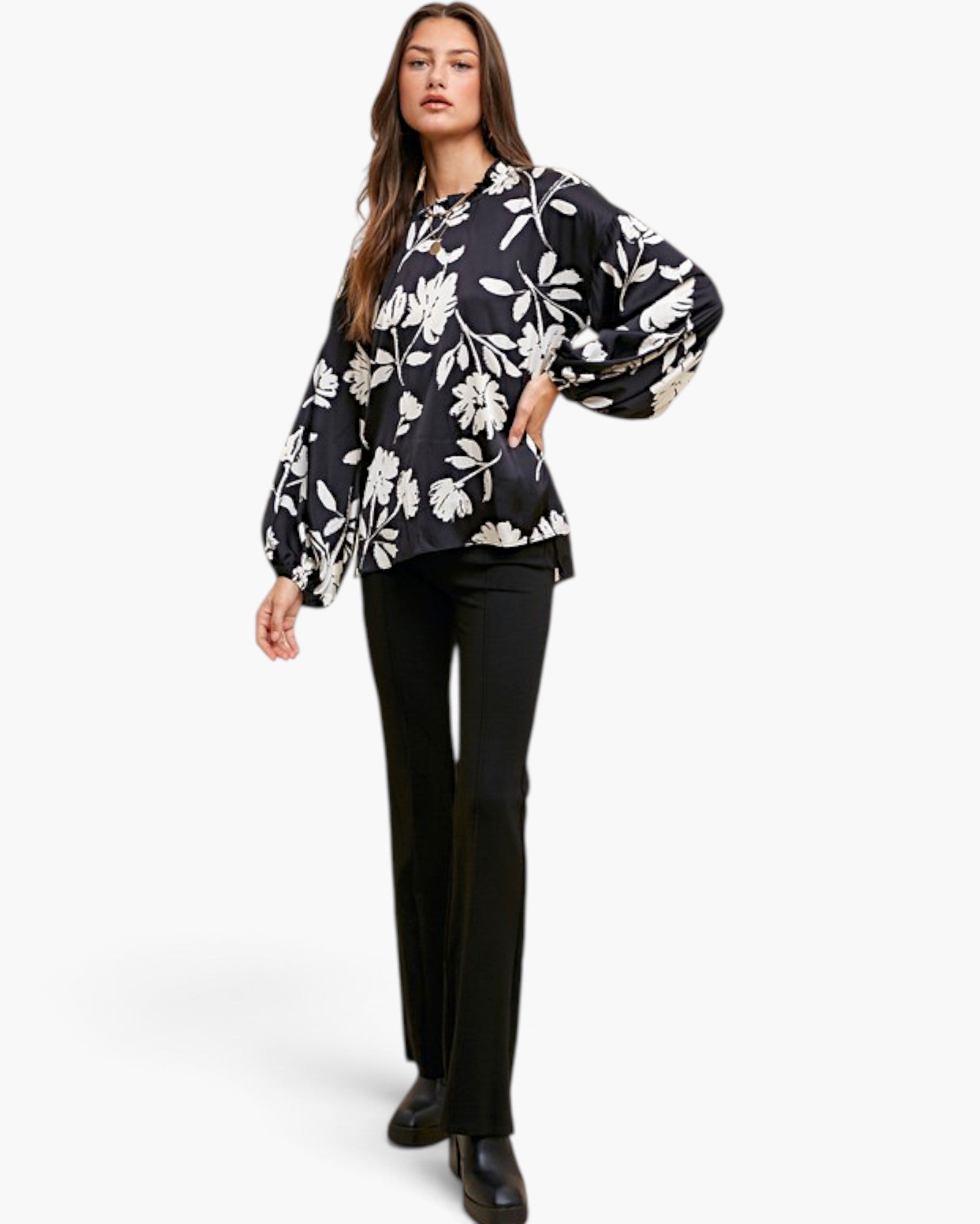 A woman modeling a black blouse with a white floral pattern and voluminous balloon sleeves, paired with black trousers, against a plain white studio background.