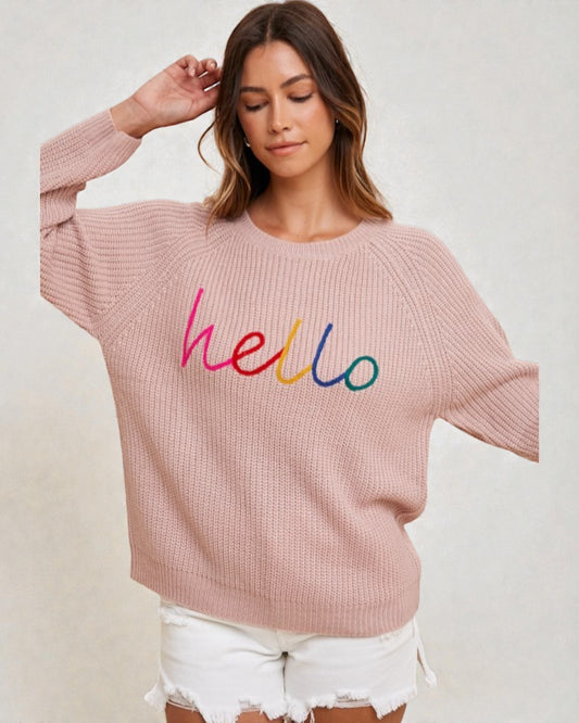 Woman wearing a pink sweater with 'hello' in colorful letters on a plain background
