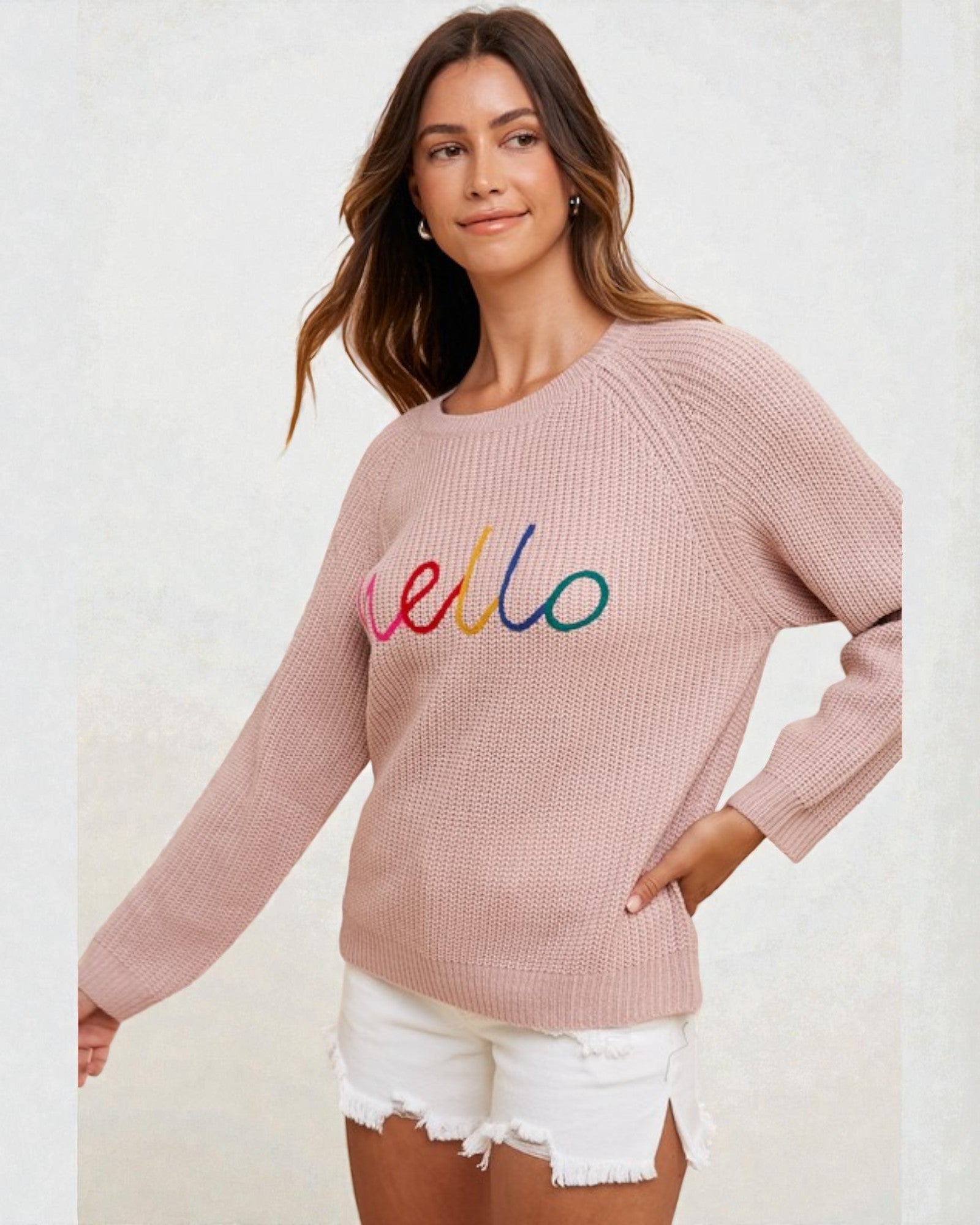 Woman wearing a pink sweater with 'hello' in colorful letters on a white background