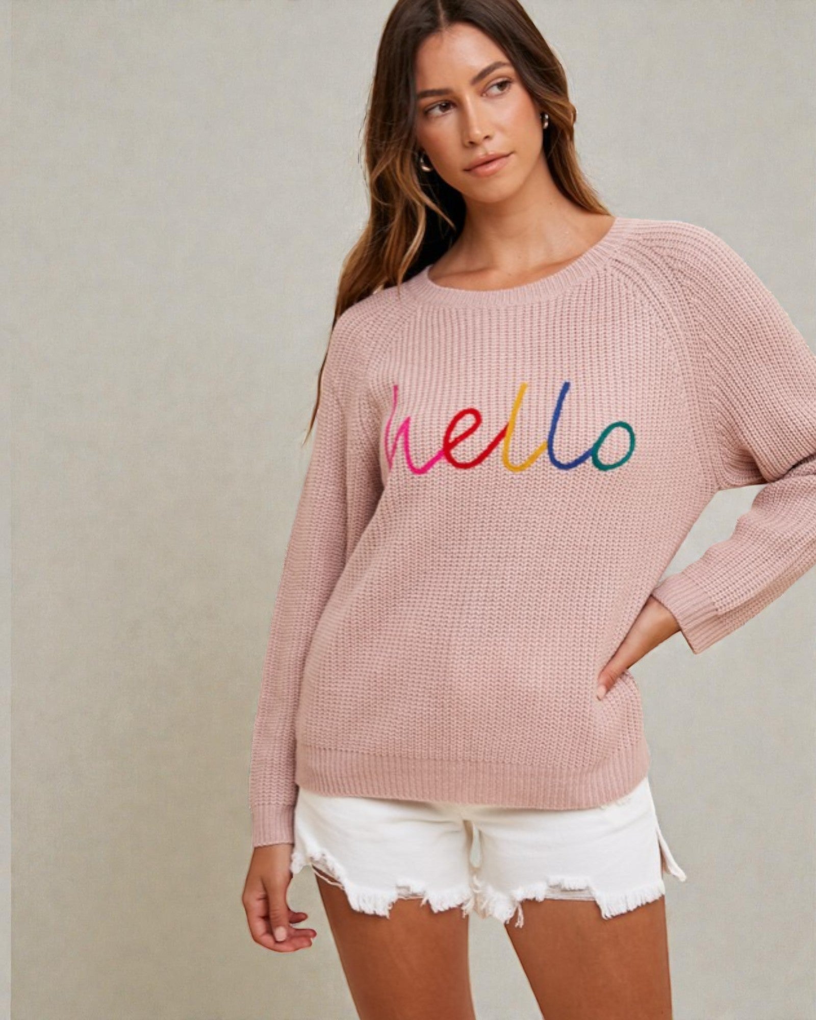 Woman wearing a pink sweater with 'hello' in colorful letters on a neutral background