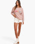 A woman modeling a light pink ribbed knit sweater with a colorful 'hello' graphic across the chest, paired with white denim shorts and white ankle boots, against a plain white background.