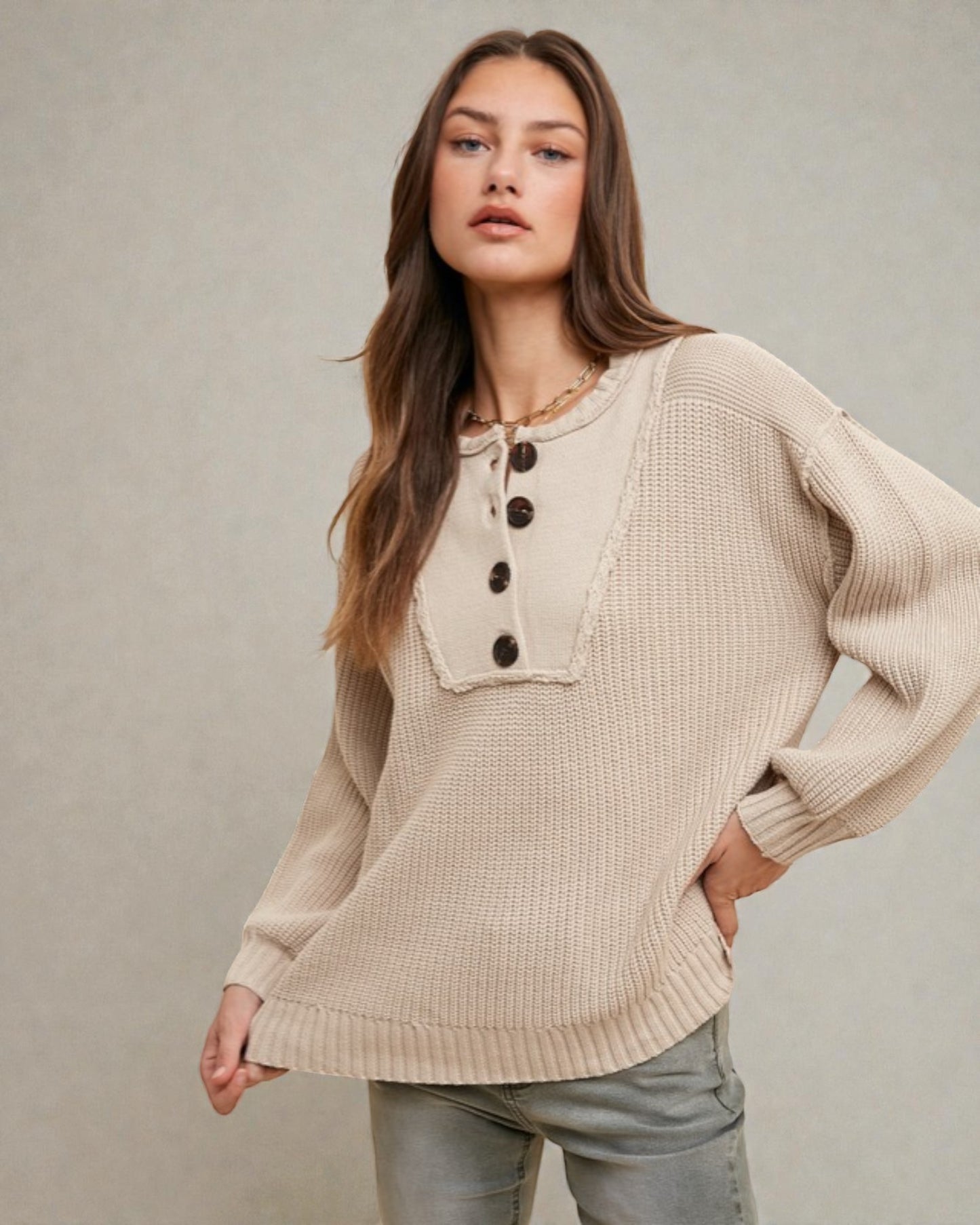 Woman wearing a beige knit sweater with button details against a neutral background