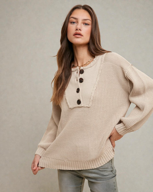 Woman wearing a beige knit sweater with button details against a neutral background