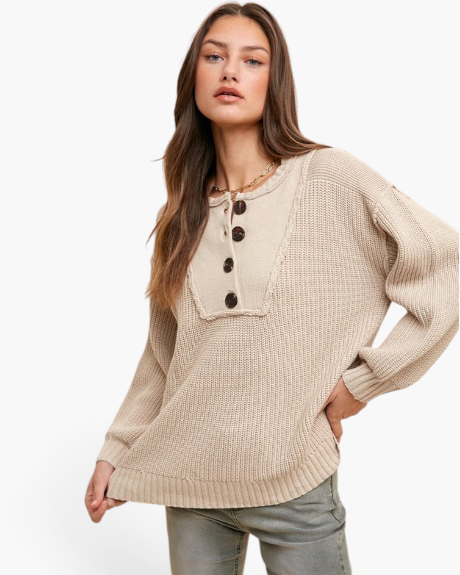 A woman wearing a beige waffle-knit sweater with a buttoned split neckline and drawstring detail, paired with gray jeans, against a plain white studio background.