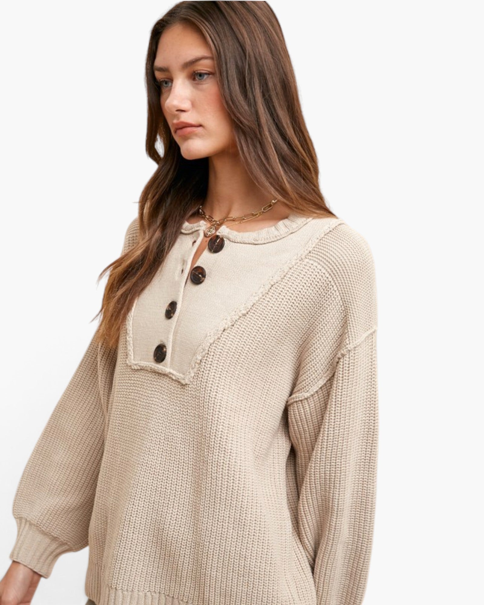 A woman wearing a beige knit sweater with a ruffled collar, dark brown buttons, and a textured waffle knit body, photographed against a clean white background.