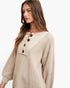 A woman wearing a beige knit sweater with a ruffled collar, dark brown buttons, and a textured waffle knit body, photographed against a clean white background.