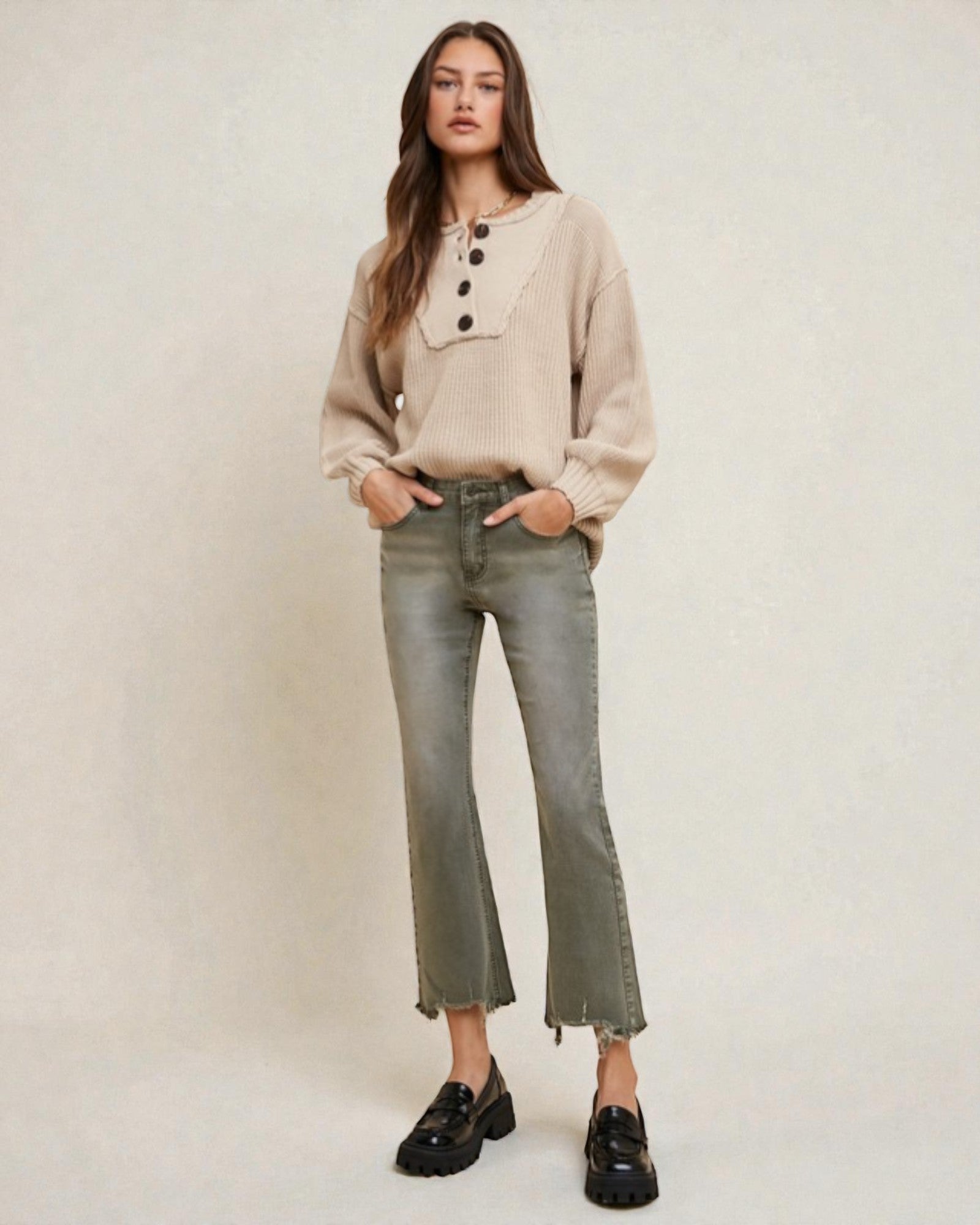 Woman wearing a beige sweater and green jeans on a plain background