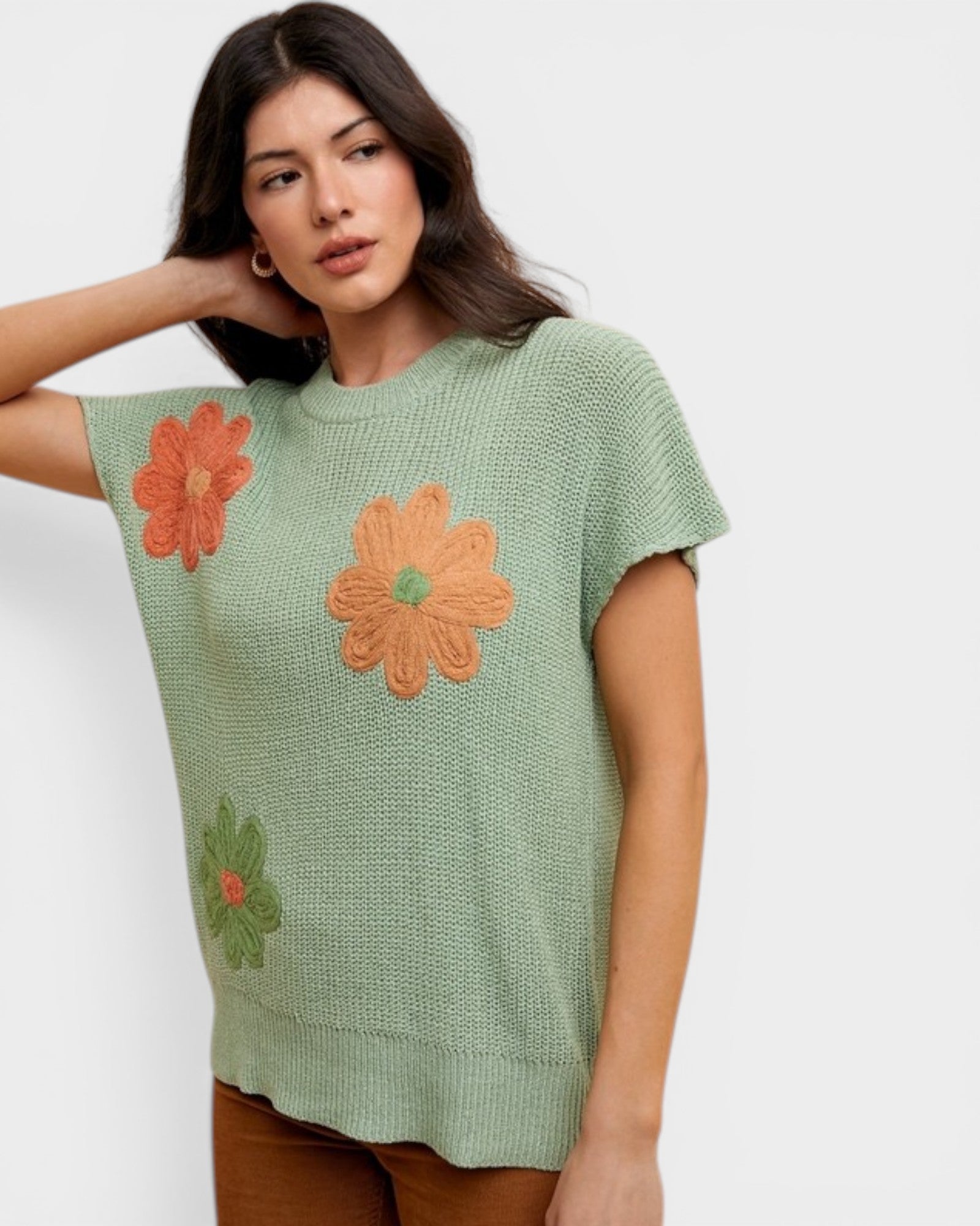 Woman wearing a green knitted top with orange floral patterns on a white background