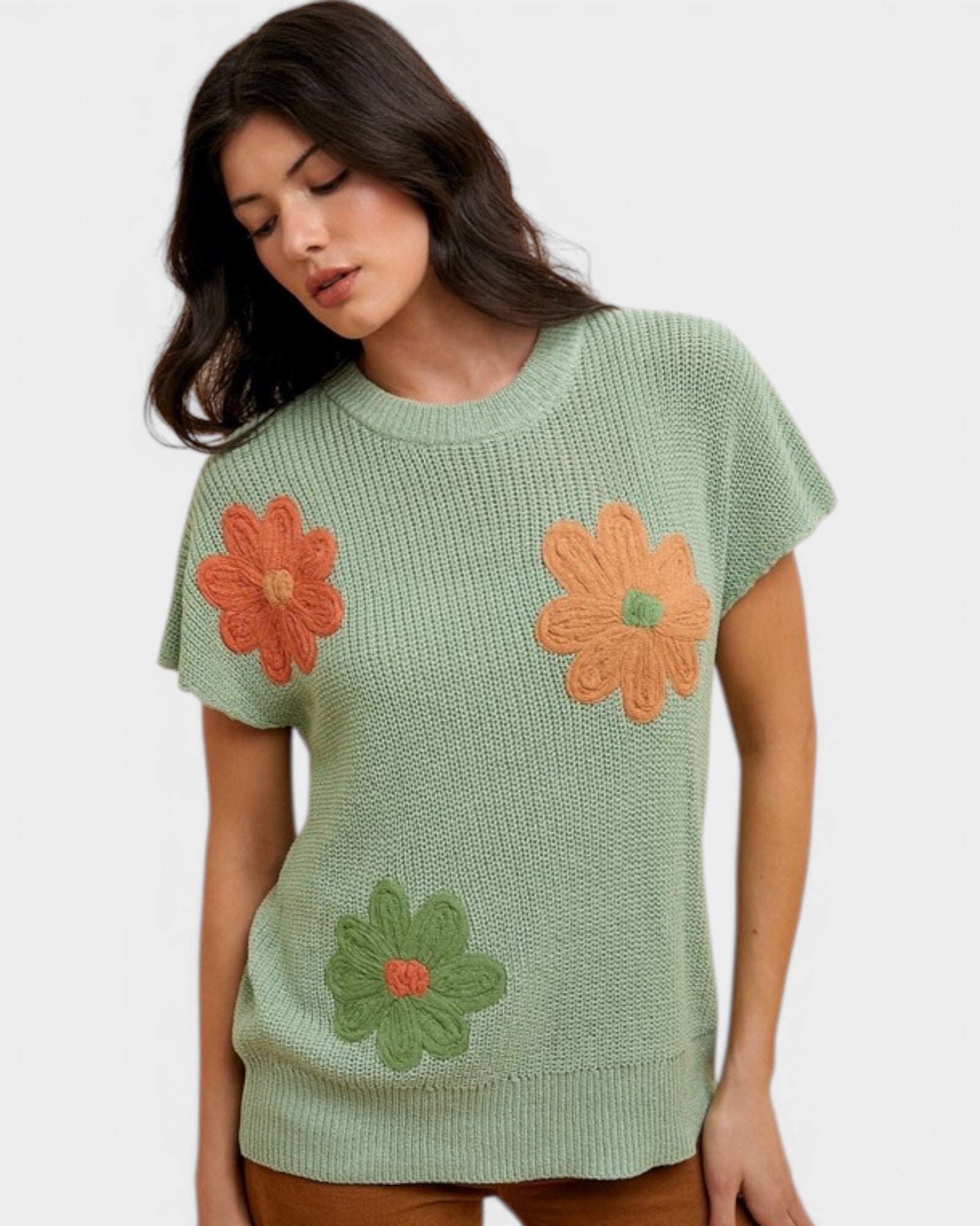 Woman wearing a green sweater with orange and green floral patterns on a white background