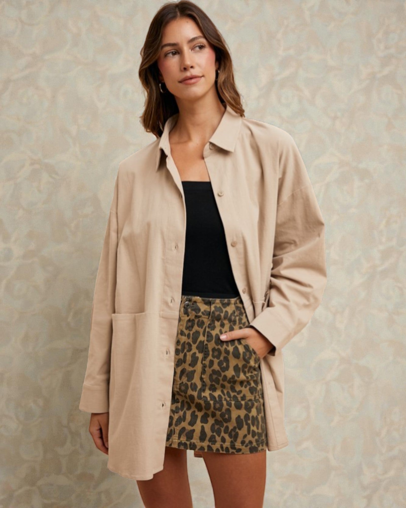 Woman wearing a beige jacket, black top, and leopard print shorts against a neutral background