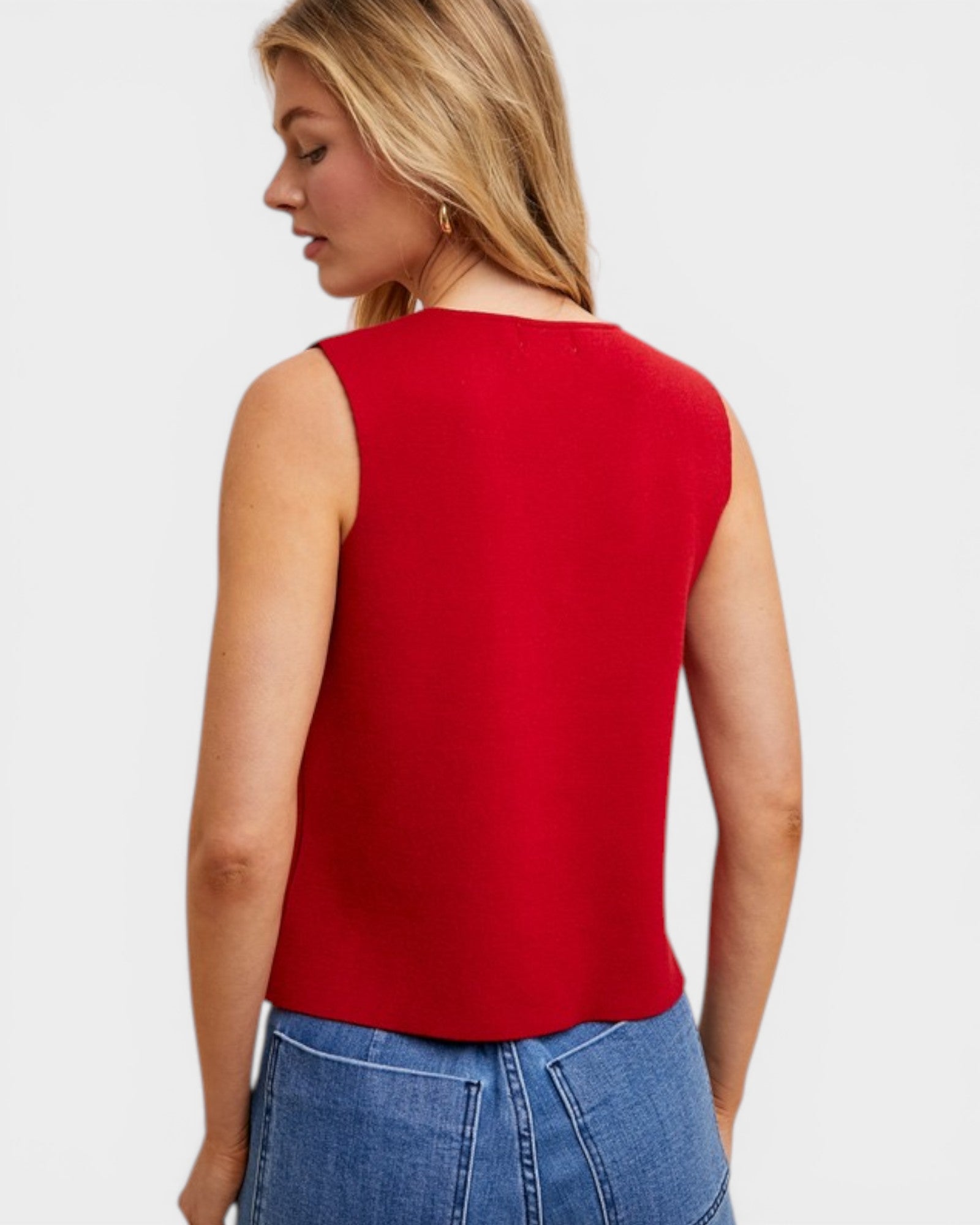 Woman wearing a red sleeveless top and blue jeans on a light gray background