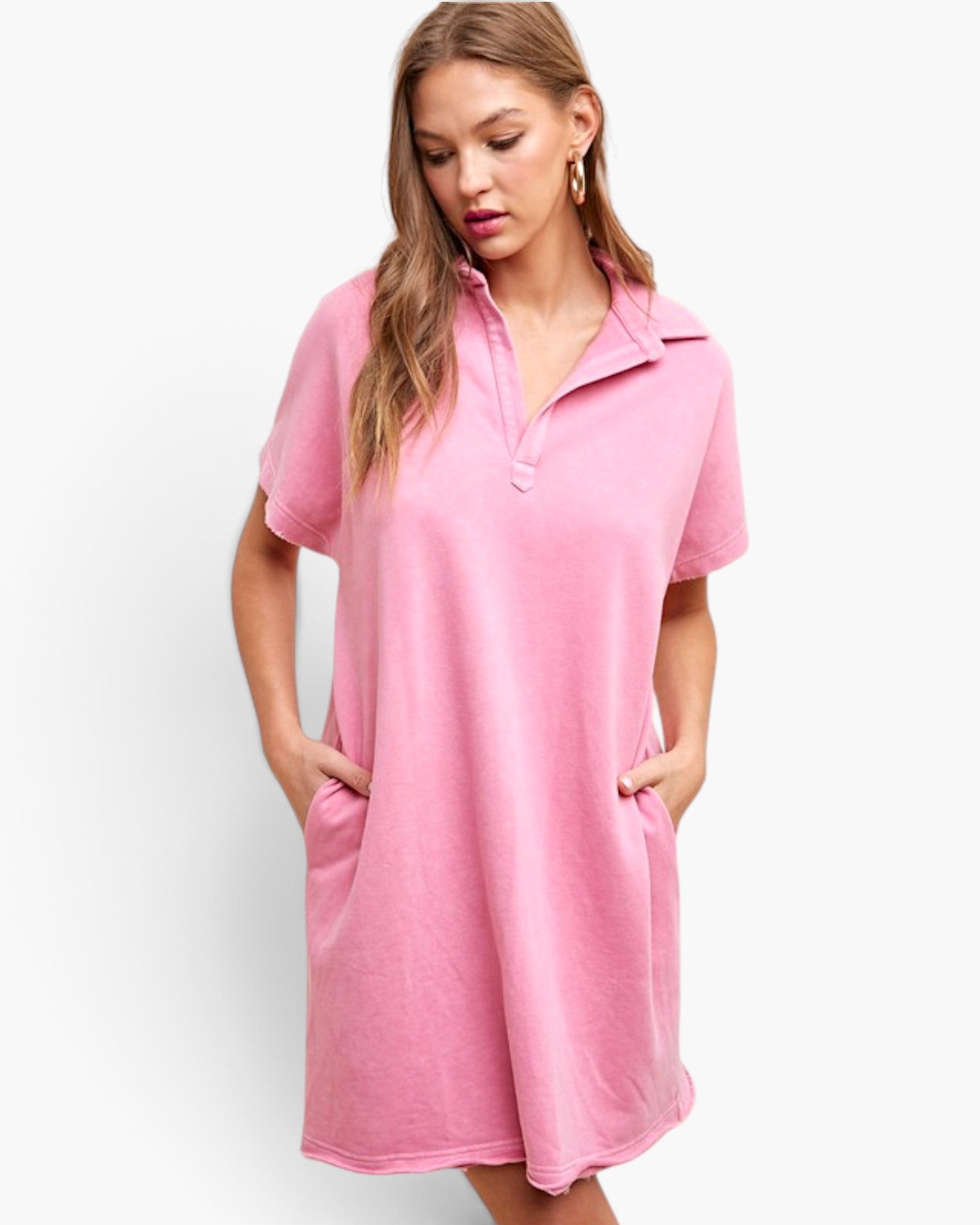 A woman wearing a pink short-sleeve polo dress with a buttoned collar and side pockets, photographed against a clean white studio background.