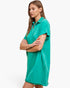 A woman modeling a short-sleeve polo shirt dress in a vibrant teal green color, standing against a plain white studio background.