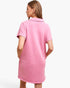 A woman shown from the back wearing a pink short-sleeve polo shirt dress against a plain white studio background.