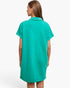 A woman viewed from the back wearing a short-sleeve collared tunic dress in a bright turquoise green color, set against a plain white studio background.