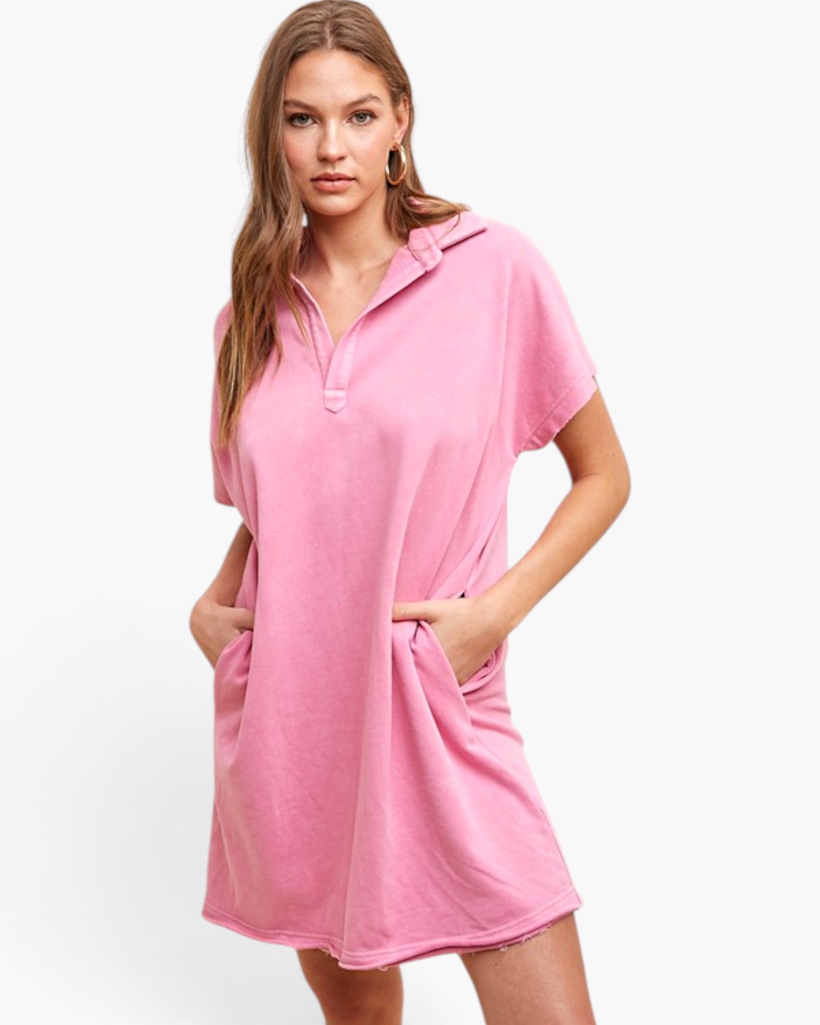 A woman modeling a pink short-sleeve polo tunic dress with a half-zip neckline and side pockets, photographed against a clean white studio background.