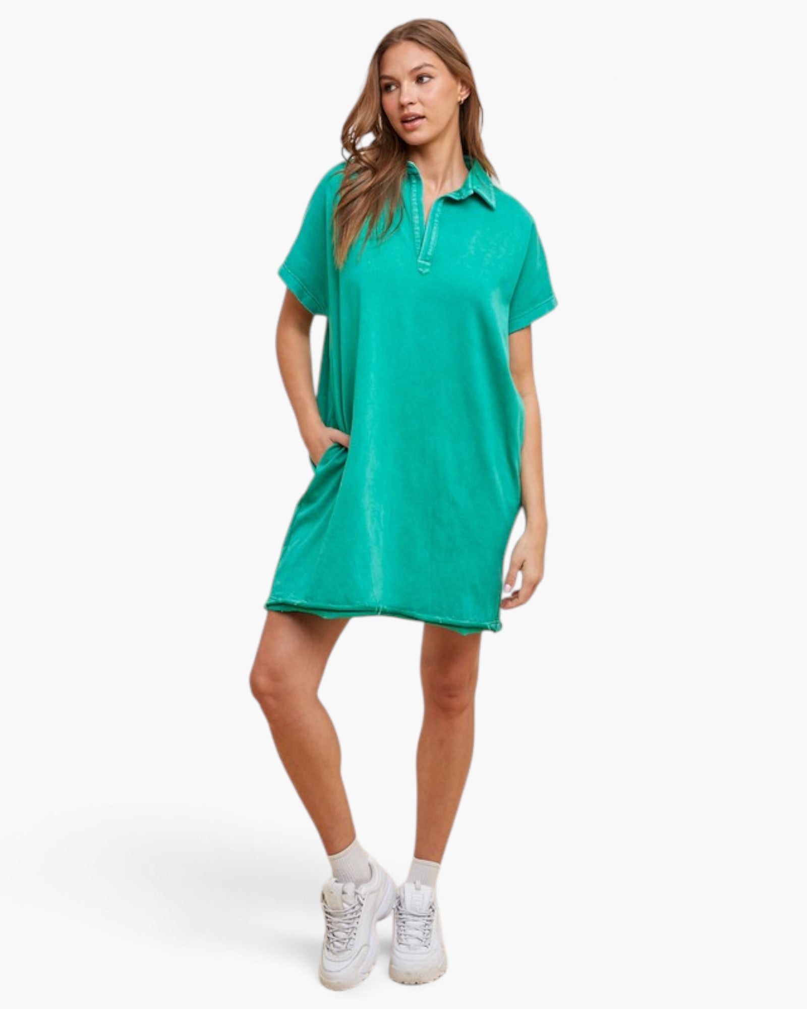 A woman modeling a short-sleeve collared polo dress in a bright turquoise green color, styled with white sneakers and socks against a clean white studio background.