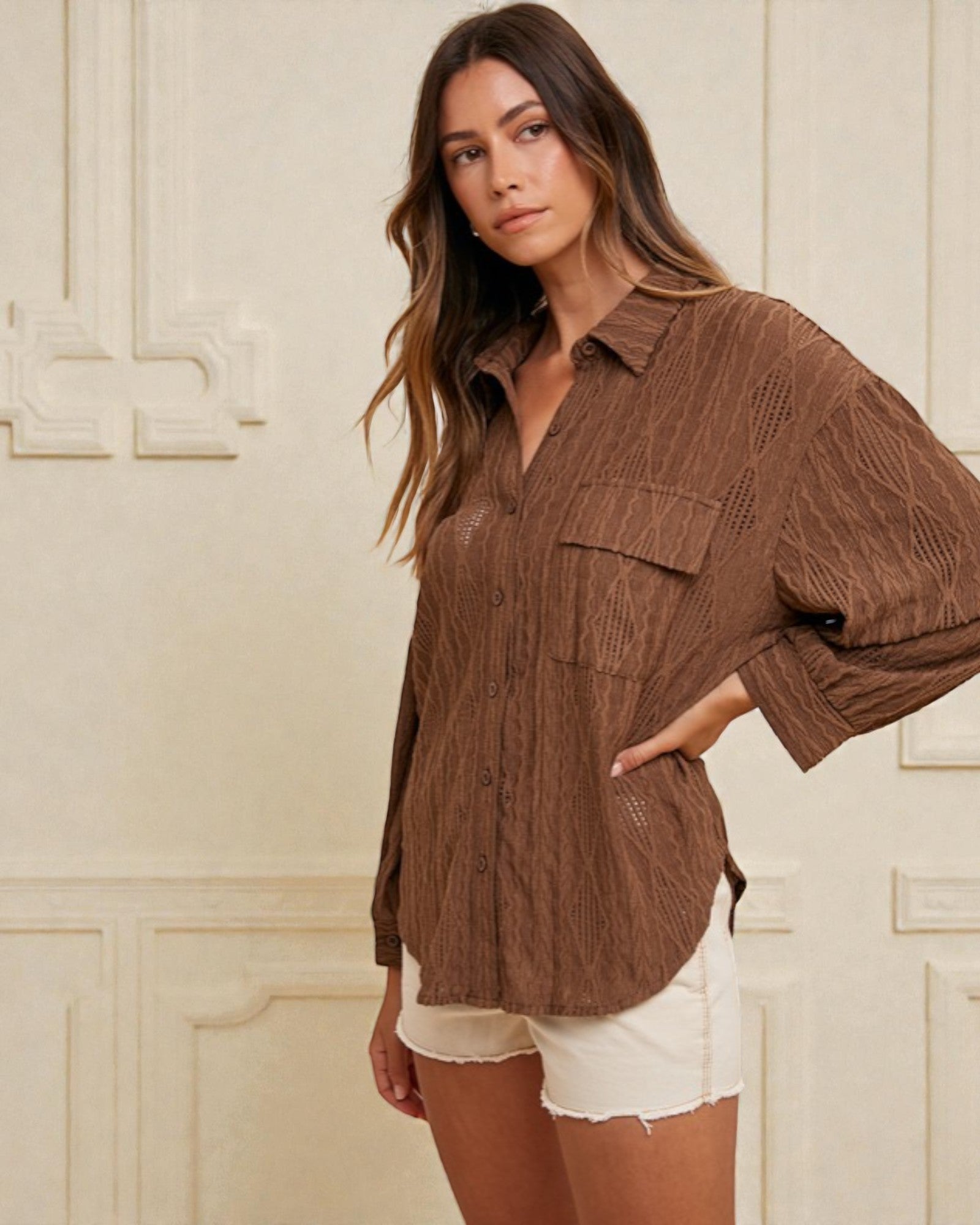 Woman wearing a brown textured shirt and white shorts against a decorative wall.