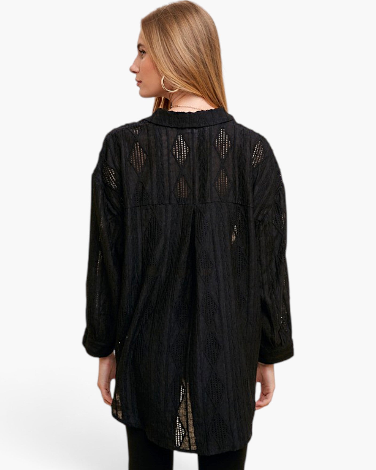 A woman shown from the back wearing a black textured long-sleeve tunic top with sheer geometric lace cutouts, set against a plain white studio background.