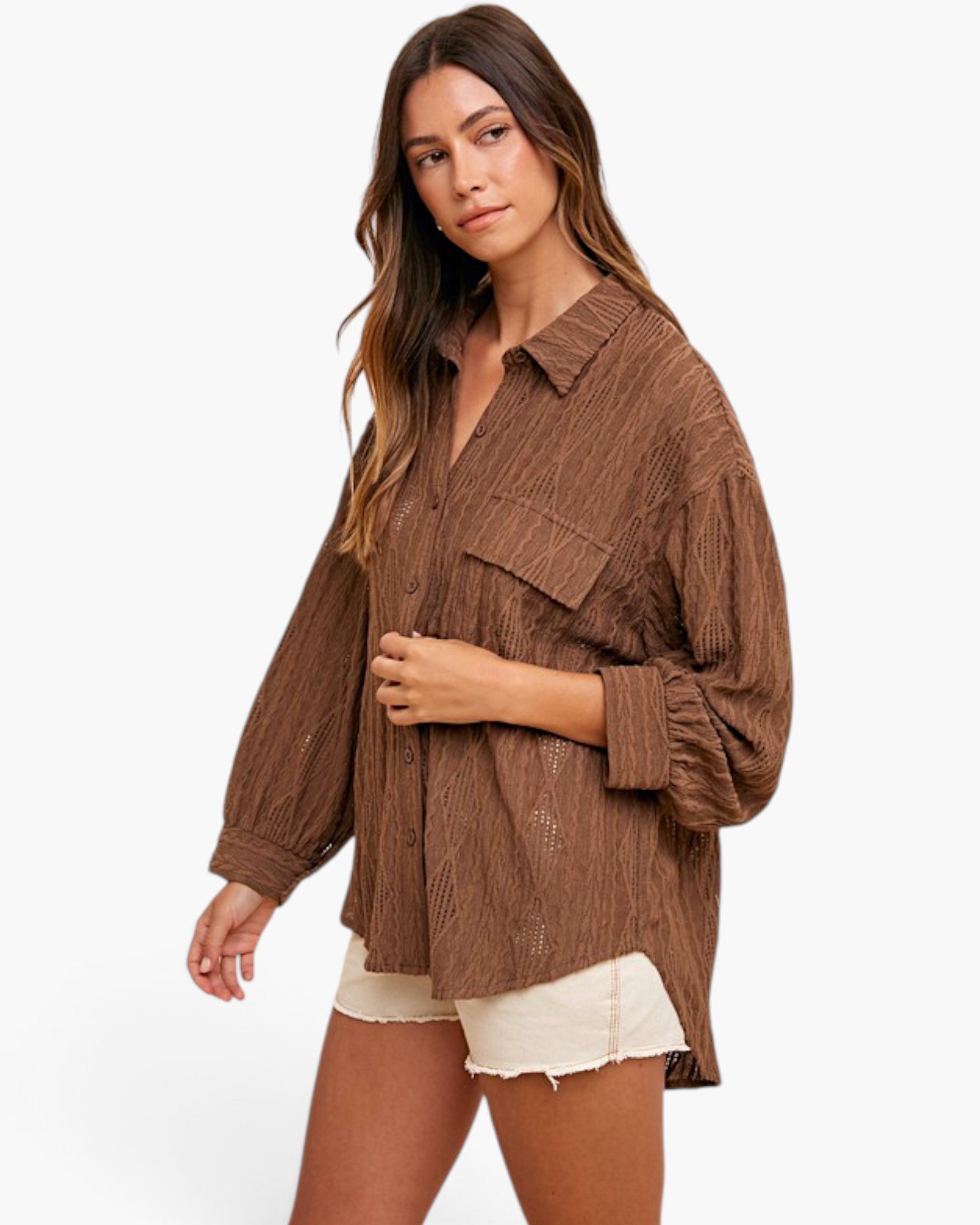A woman modeling a brown crinkled button-up shirt with long sleeves and chest pockets, paired with off-white shorts, against a plain white background.