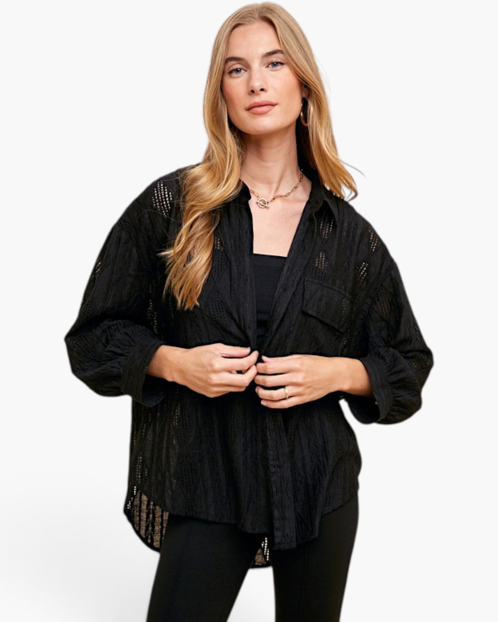 A woman modeling a black open-front long-sleeve shirt with textured, semi-sheer eyelet lace details on the shoulders and sides, worn over a black top and black pants against a plain white background.