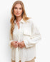 A woman wearing a textured, off-white long-sleeve button-up shirt with a chest pocket, photographed against a clean white studio background.