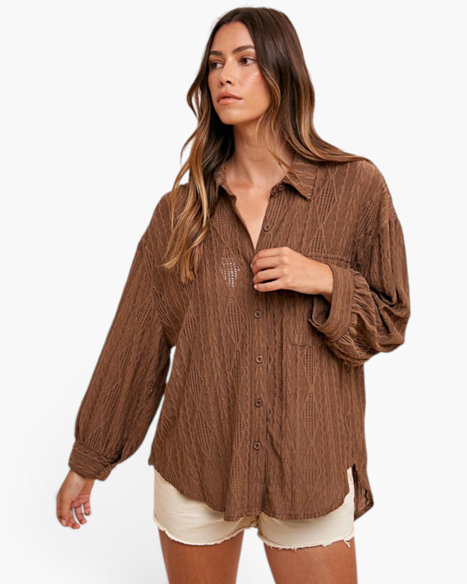 A woman modeling a brown crinkled button-up shirt with long sleeves and cream shorts against a plain white background.