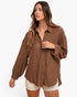A woman modeling a brown crinkled button-up shirt with long sleeves and cream shorts against a plain white background.