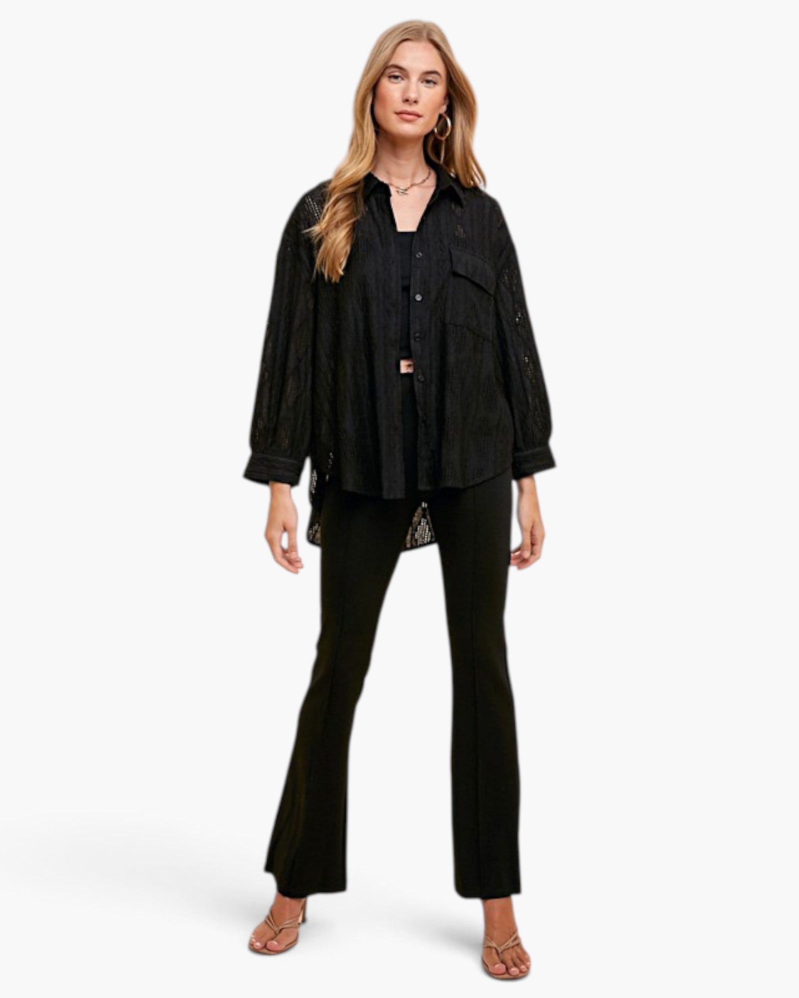 A woman modeling a black textured button-up shirt and matching black flared pants against a light gray studio background.