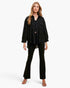 A woman modeling a black textured button-up shirt and matching black flared pants against a light gray studio background.